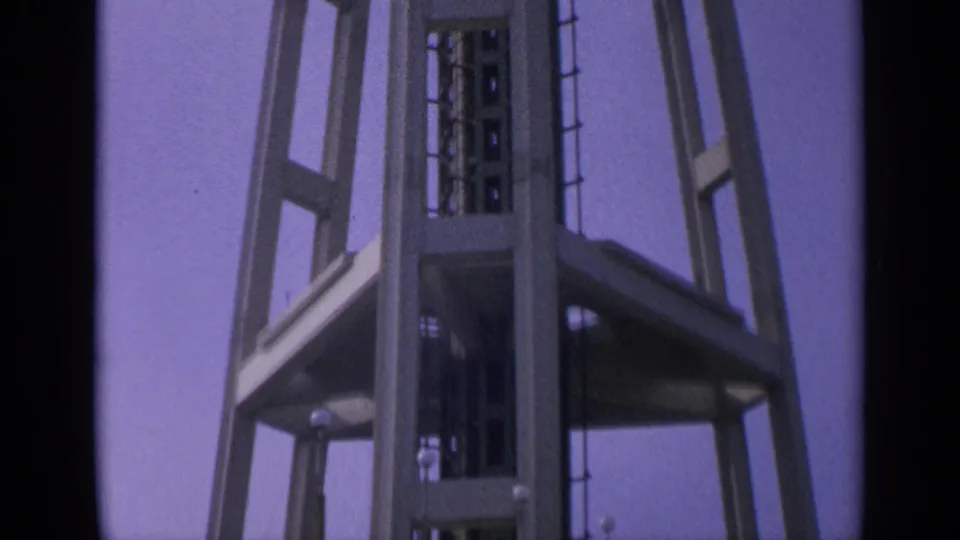 Visitor-shot 1963 8mm frame showing the Space Needle's lower supports and shaft against pale blue sky.