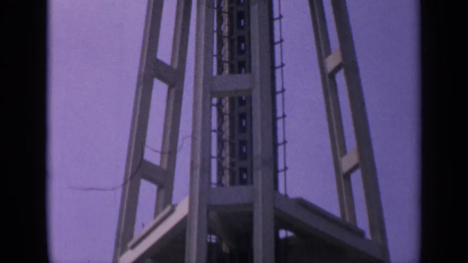 1960s home-movie frame of the Space Needle's lower-to-mid structure, with visible grain and faded color.