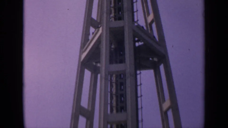 1963 8mm frame showing a low-angle Washington tower view with steel supports and deck structure against a purple sky.