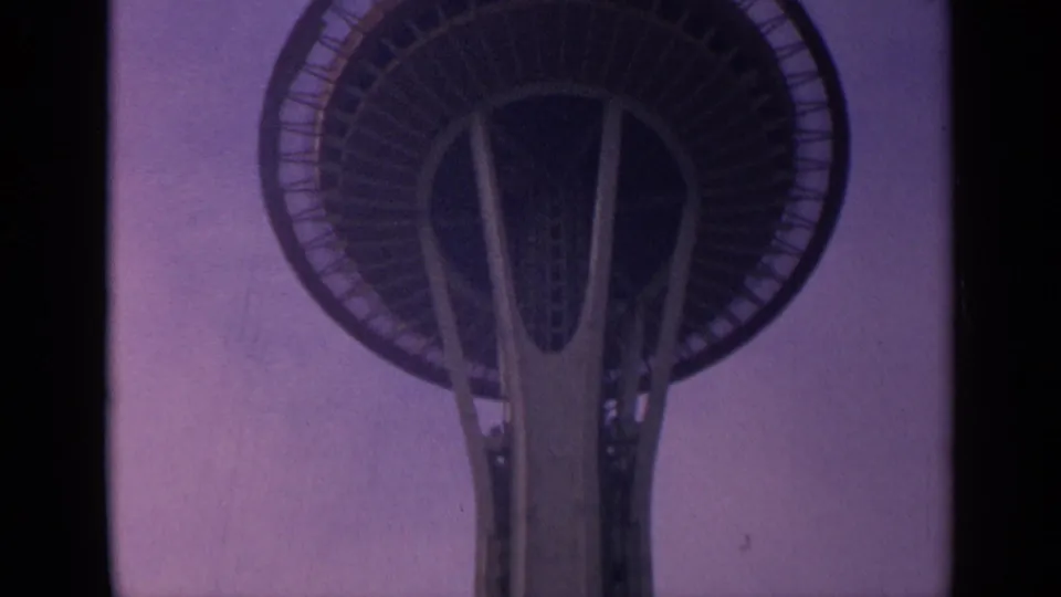 1963 8mm frame of the Space Needle observation deck looming above the central shaft in a low-angle Seattle view.