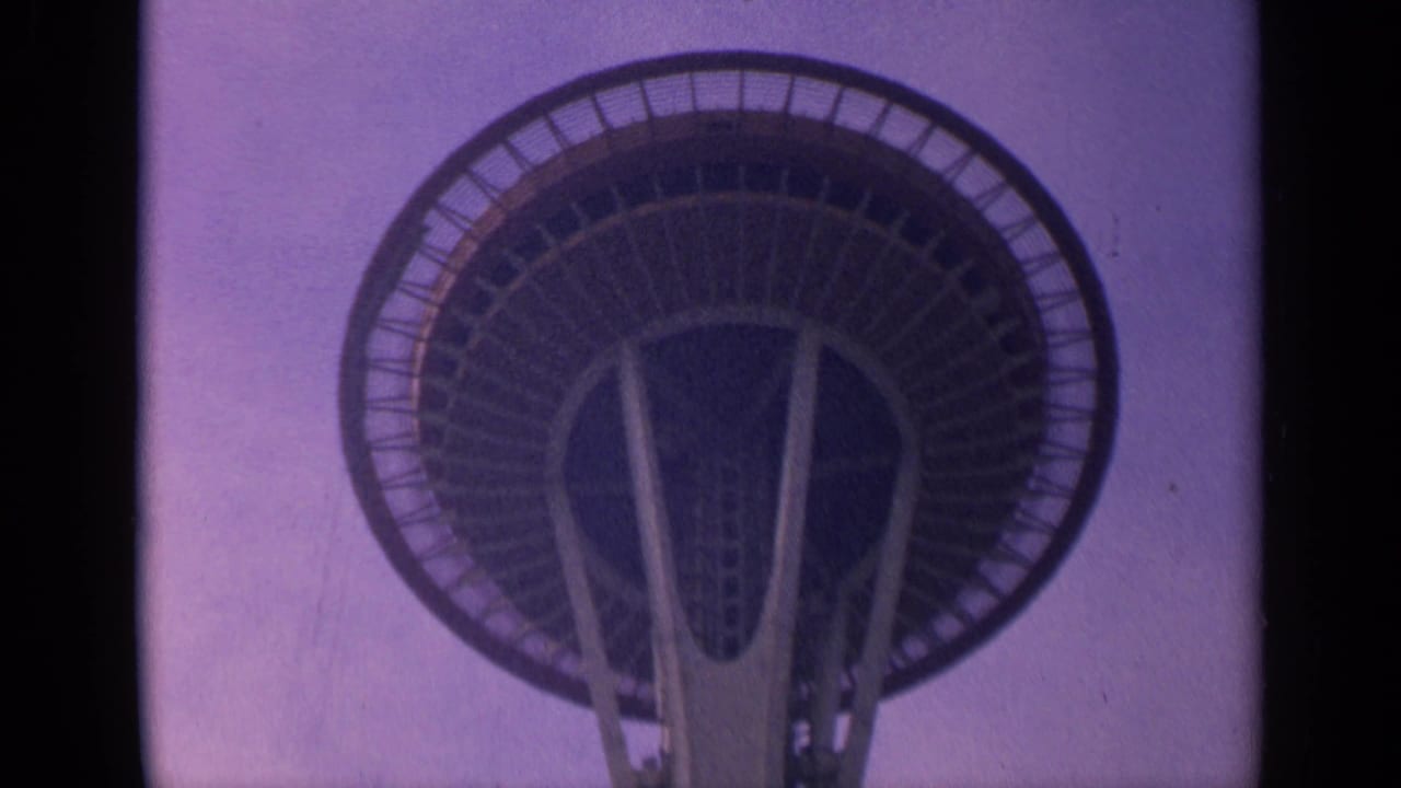 1963 Washington 8mm frame showing the Space Needle observation deck from below against a purple-tinted sky.