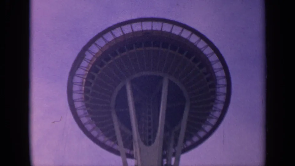 1963 Washington home-movie frame with the Space Needle circular deck and support structure filling the view.