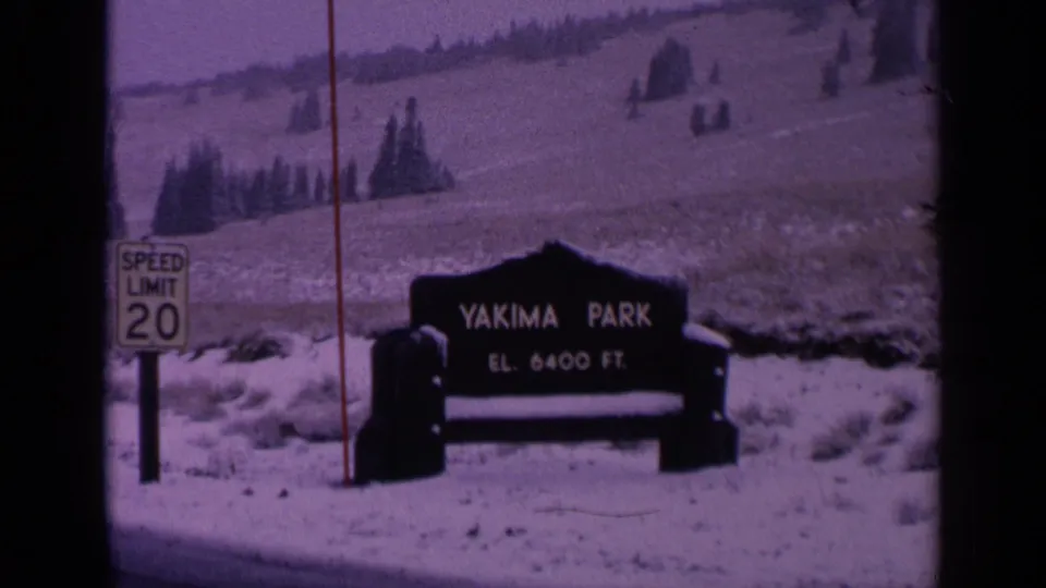 1963 Washington frame of the Yakima Park sign and elevation text, filmed from a roadside with snow, evergreens, and visible 8mm frame edges.