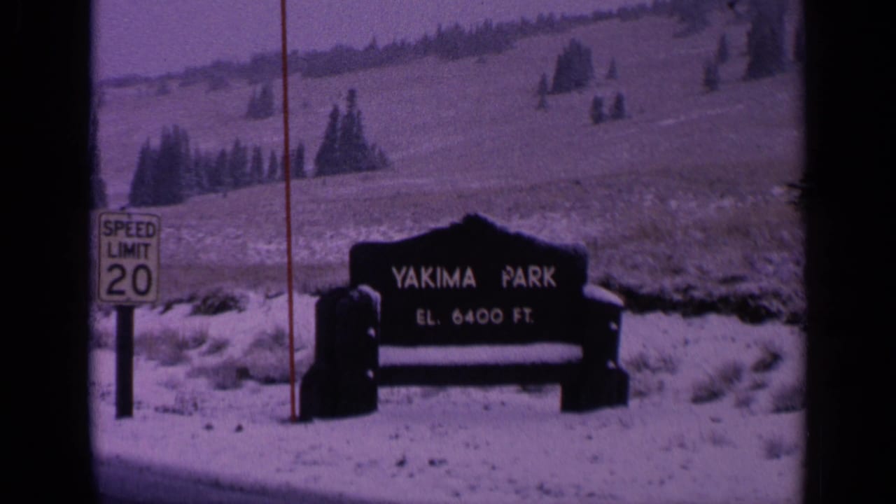 1963 Washington home-movie frame showing Yakima Park signage in a snowy mountain setting, with speed limit marker and visible film grain.