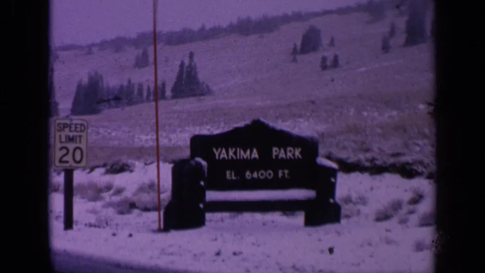 1963 Washington 8mm frame showing a Yakima Park sign, speed-limit sign, snow, open slopes, and dark film borders.