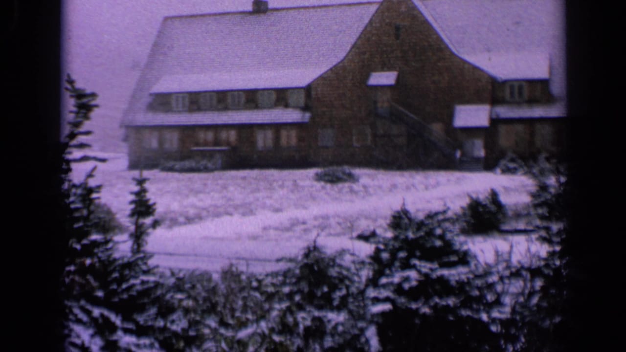 1963 Washington 8mm frame showing a broad lodge facade, snowy roof, foreground evergreens, and soft purple film color.