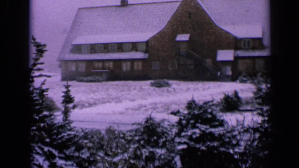 1963 Washington 8mm frame showing a broad lodge facade, snowy roof, foreground evergreens, and soft purple film color.