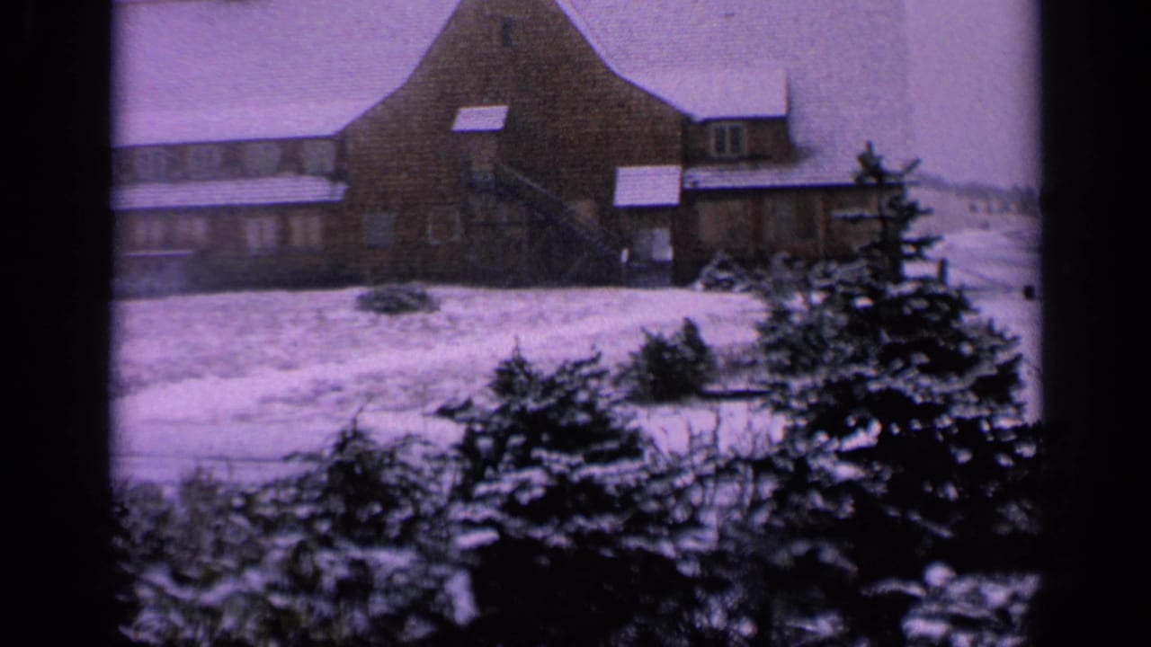 1963 Washington 8mm frame showing a large snow-covered farmhouse, evergreen shrubs, and a pale winter field.