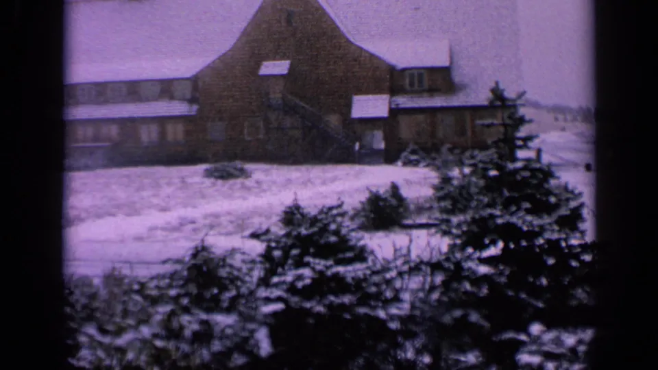 1963 Washington 8mm frame showing a large snow-covered farmhouse, evergreen shrubs, and a pale winter field.