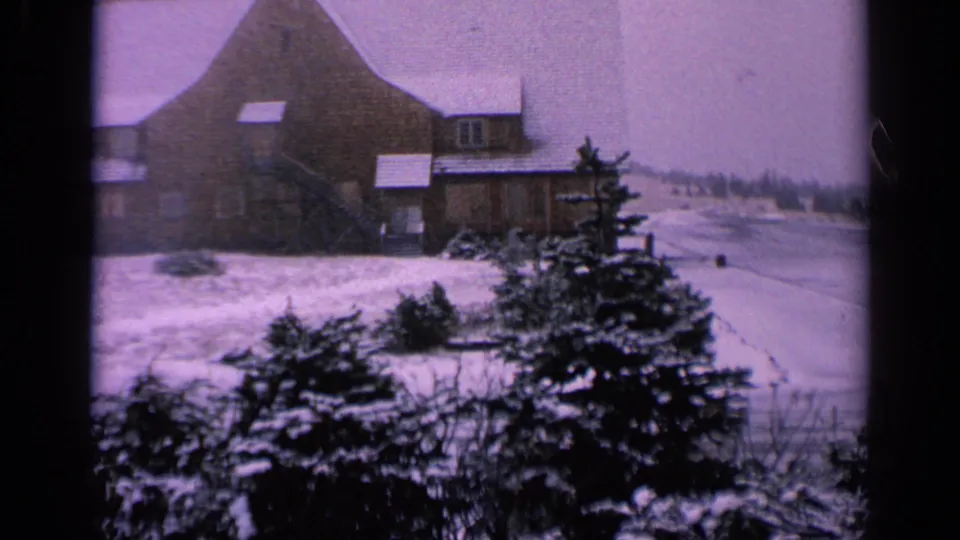 1963 Washington home-movie frame with the farmhouse partly centered and snow-covered land opening toward a distant treeline.