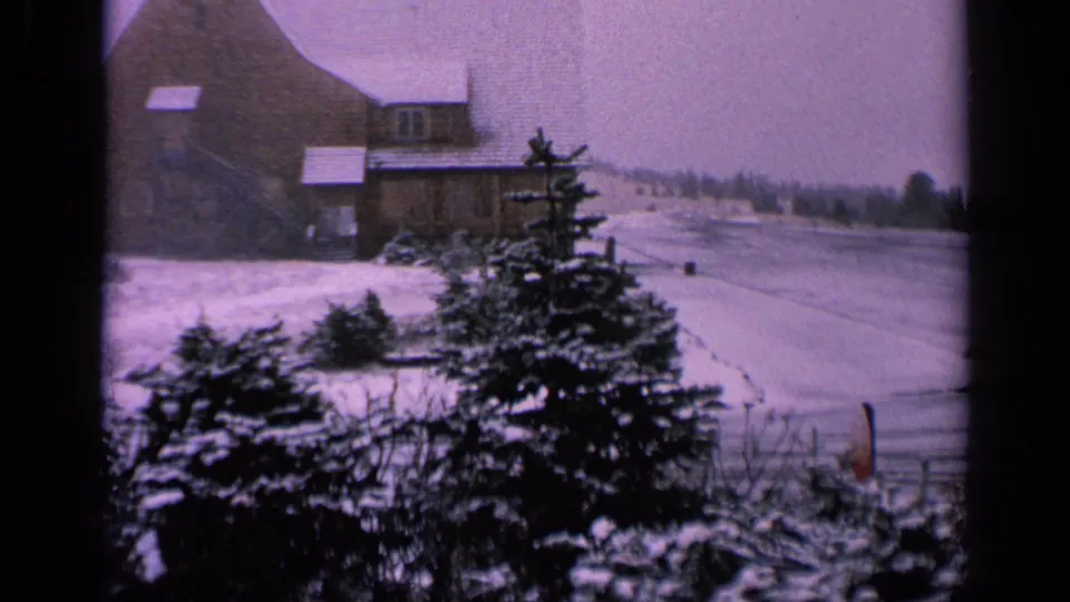 1963 Washington 8mm frame showing snowy evergreens, part of the farmhouse, and a frozen pond or waterway beyond.