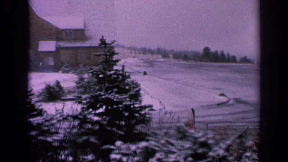 1963 Washington winter frame with an evergreen tree, frozen pond or waterway, distant treeline, and farmhouse partially visible at left.