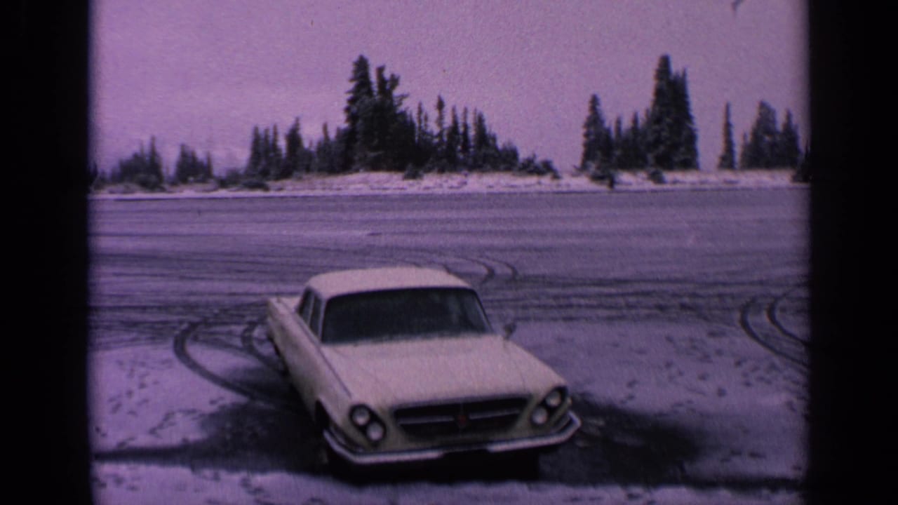 White car parked on a frozen Washington road in 1963, seen with snowy tire marks and a line of evergreens under a pale sky.