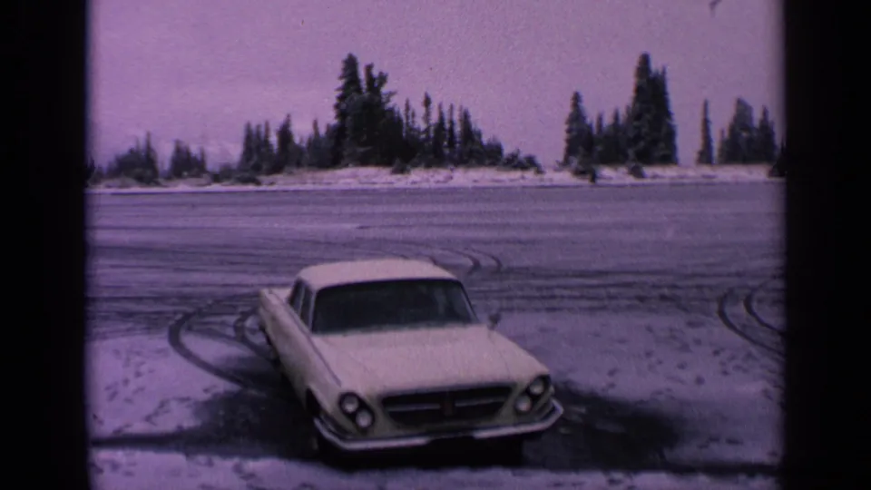 White car parked on a frozen Washington road in 1963, seen with snowy tire marks and a line of evergreens under a pale sky.