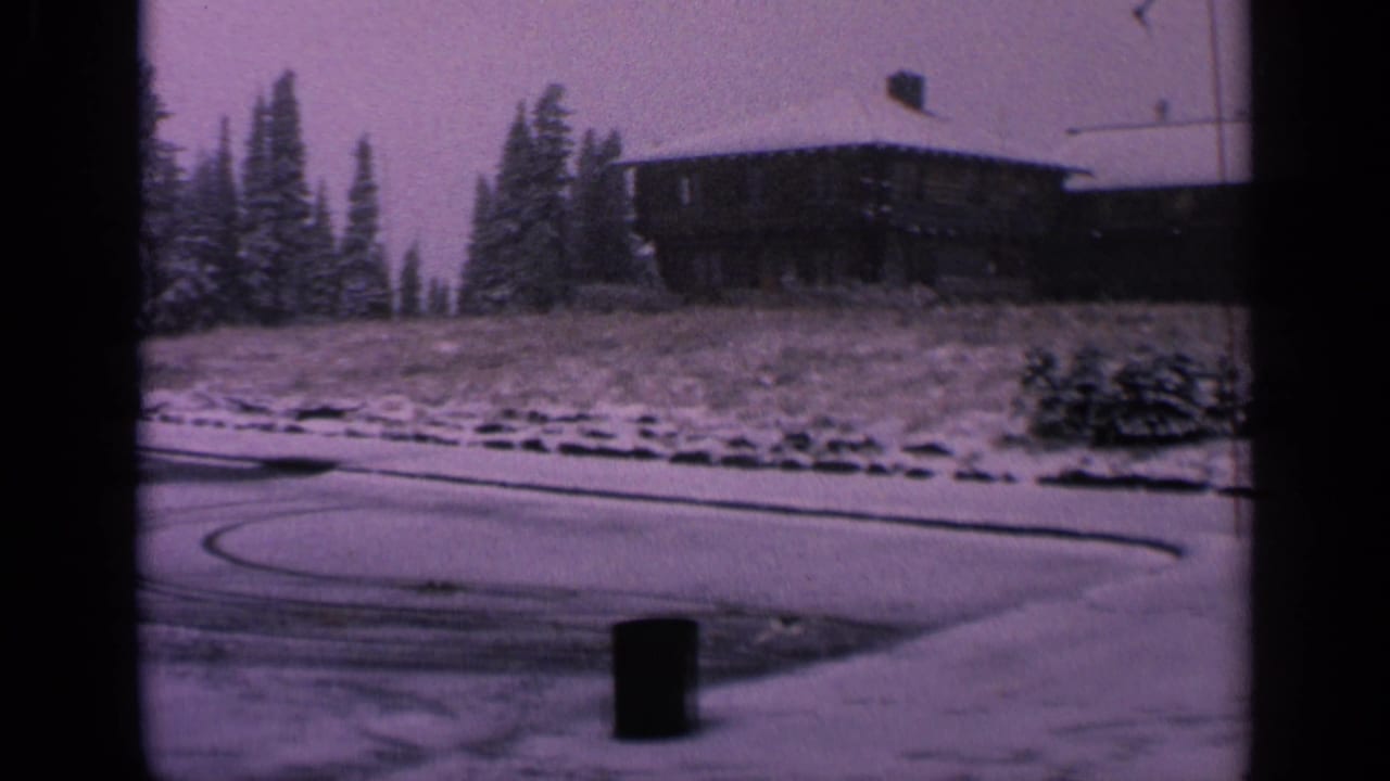 1963 Washington 8mm frame centered on snow, tire arcs, evergreens, and a rustic-looking building above the parking lot.