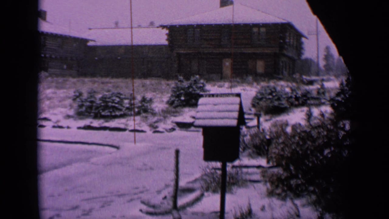 1963 Washington frame showing a quiet snow-covered neighborhood with a mailbox, shrubs, road, and log-style houses.