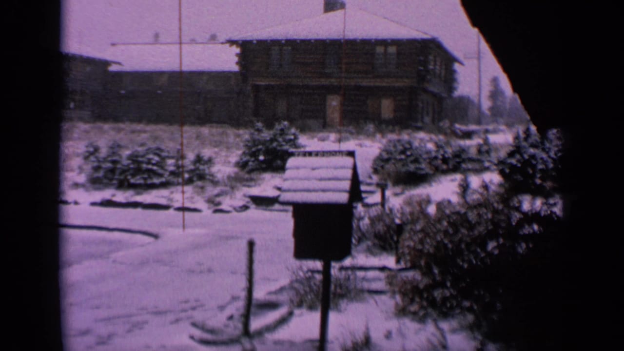 Snow-covered building and mailbox seen through dark film gate edges.