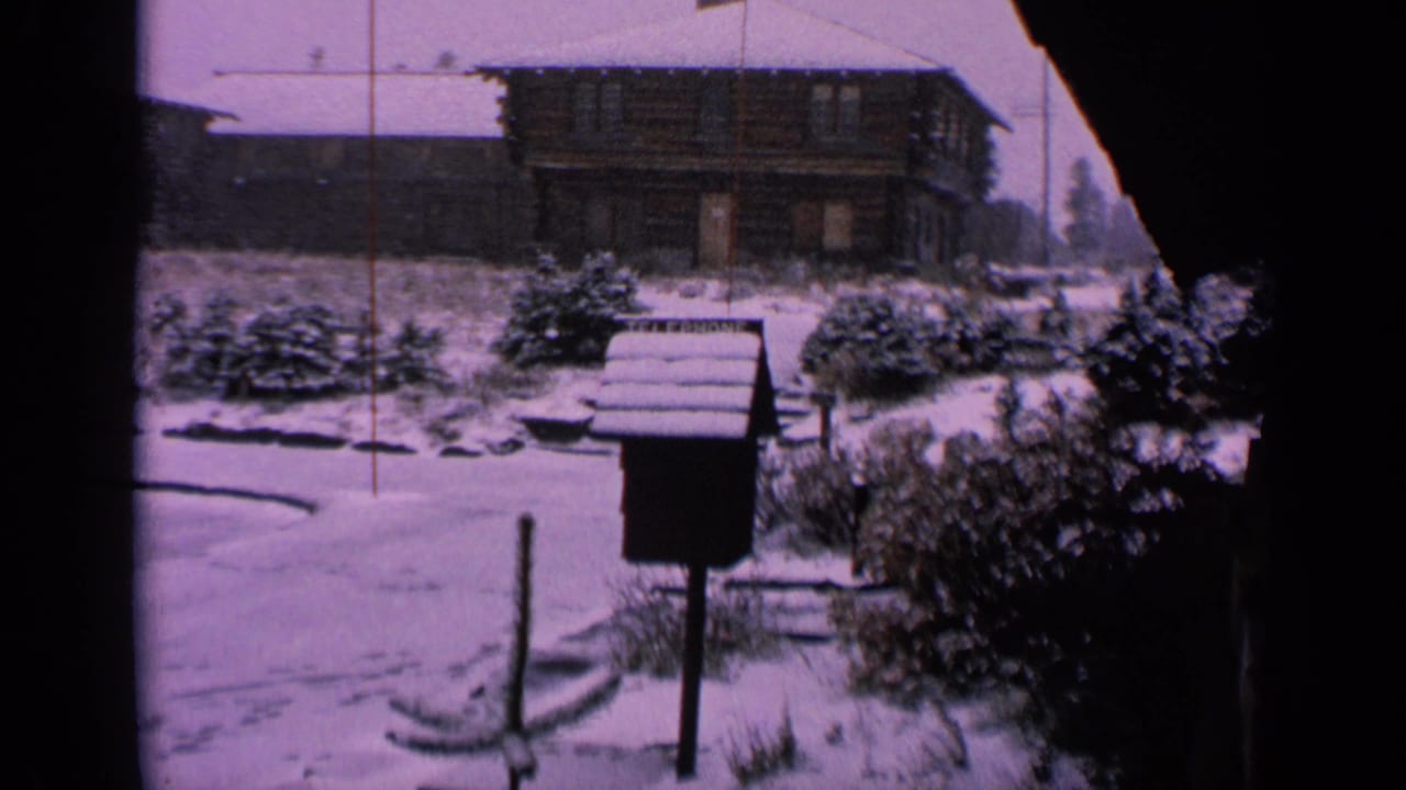 1963 Washington winter frame with a mailbox, snow-covered shrubs, and a building beyond the yard.