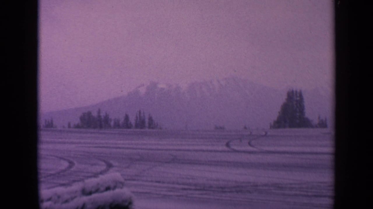 1963 Washington 8mm landscape showing tire tracks across snow, distant trees, and hazy mountain forms.