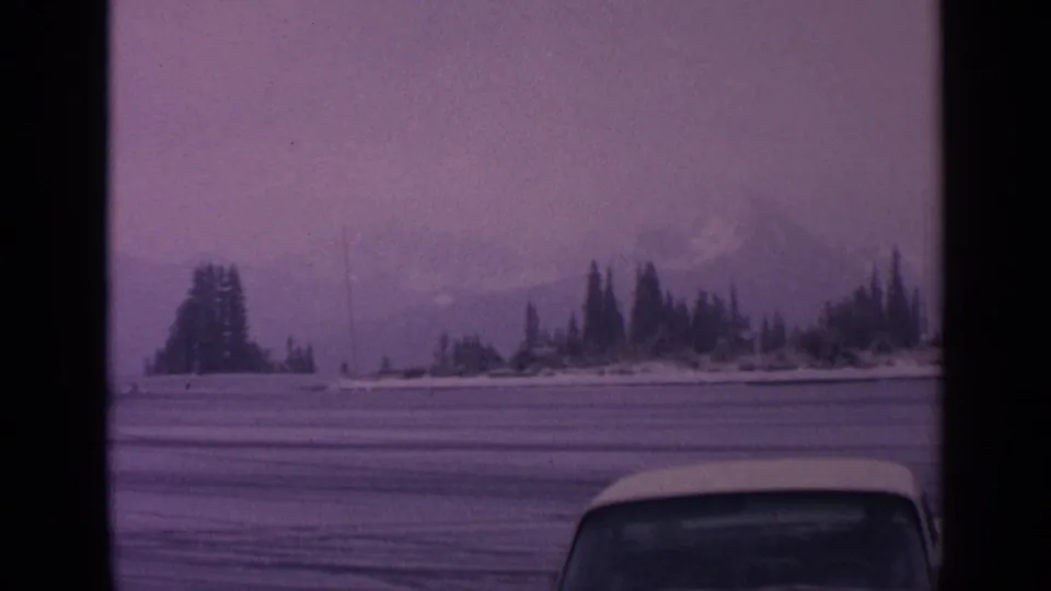 1963 Washington 8mm frame showing a purple-tinted snowy field, evergreens along the horizon, low mountains, fog, and a car roofline.