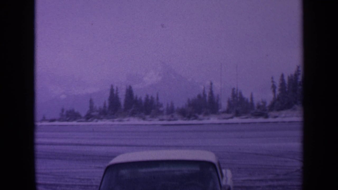 Snowy evergreen shoreline with a faint mountain and partial vehicle roof in the foreground.