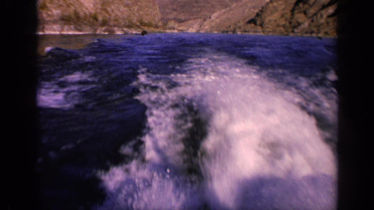 1963 Washington river view from a moving boat, with foamy wake, dark water, rocky banks, and 8mm color shift.
