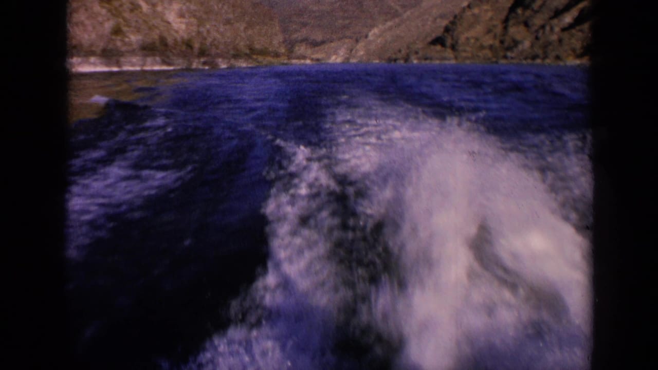 1963 Washington 8mm still with bright wake filling the lower frame and rippling dark water leading to a rocky shore.