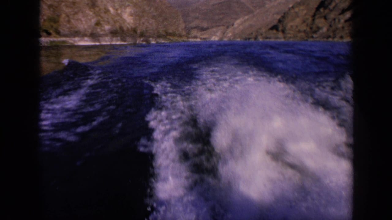 Rear-facing 1963 Washington river view with white wake cutting through deep blue water and rocky hills along the shore.