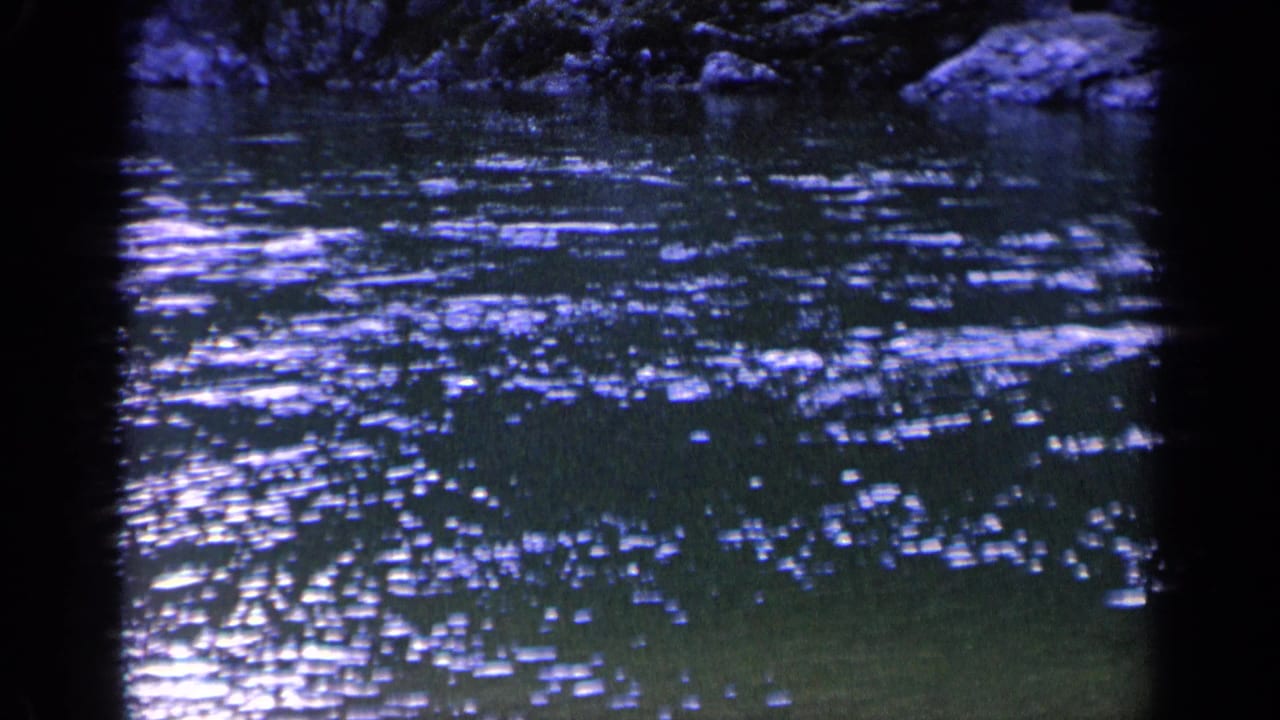 1963 Washington 8mm frame of dark rippling river water with shimmering highlights, rocks, foliage, and visible film color shift.