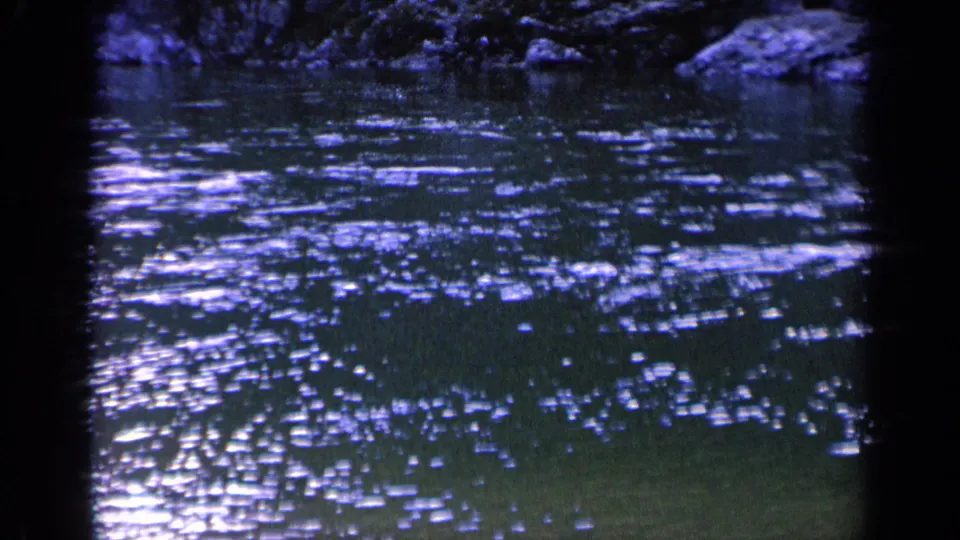 1963 Washington 8mm frame of dark rippling river water with shimmering highlights, rocks, foliage, and visible film color shift.