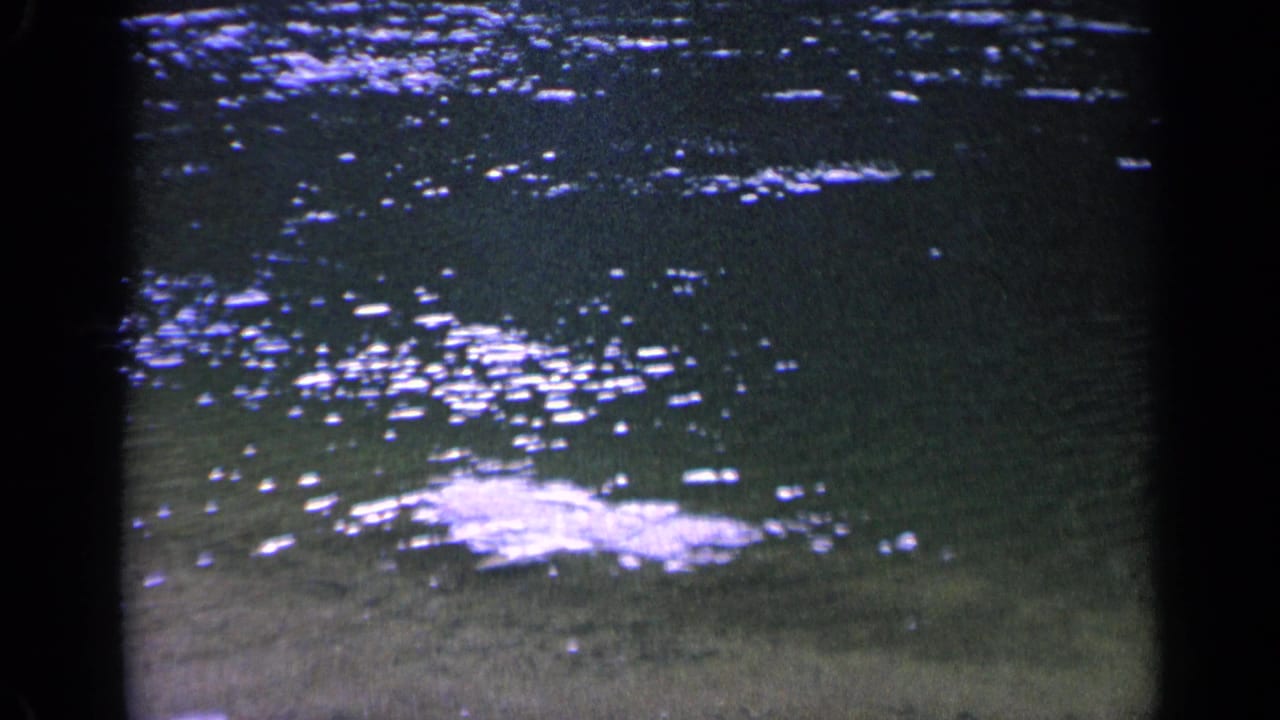 1963 Washington 8mm frame showing a bright splash-like disturbance on pond water, surrounded by ripples and scattered sunlight reflections.
