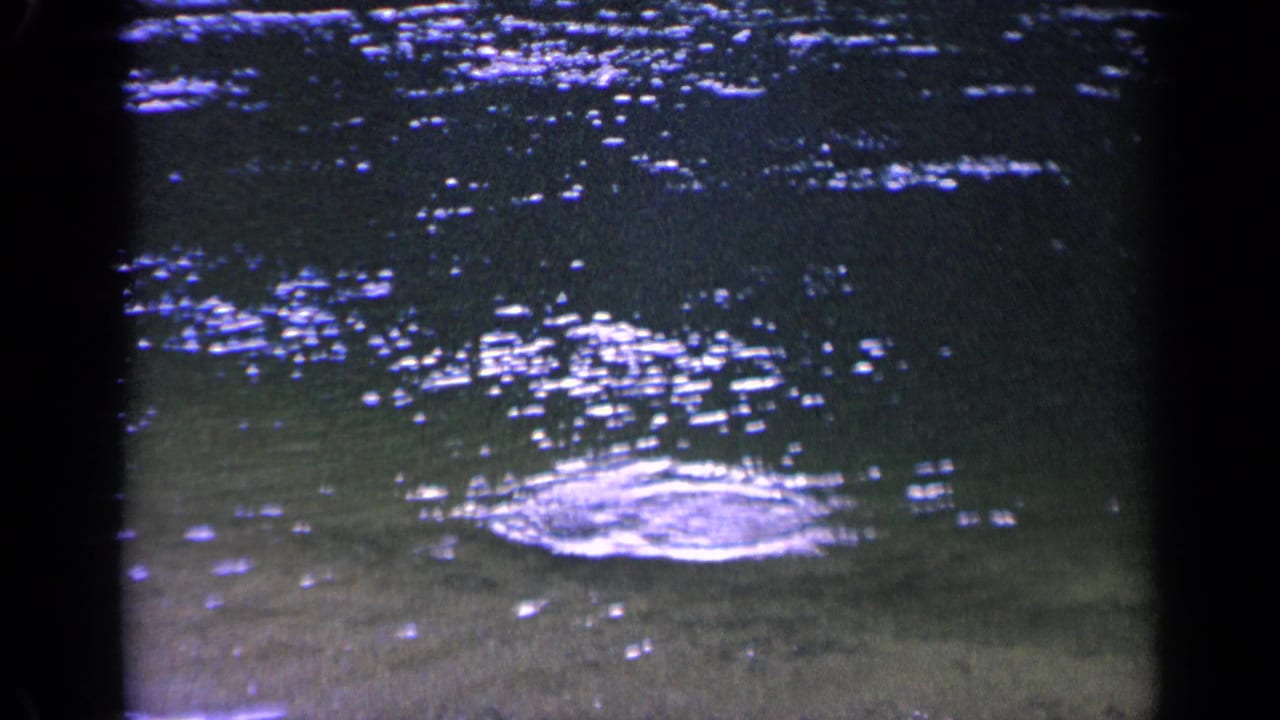 Shallow water with bright ripples and a small circular splash near the sandy bottom.