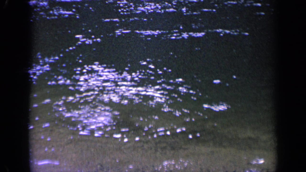Vintage 8mm frame from Washington showing rippling shallow lake water with bright reflected highlights over a sandy bottom.