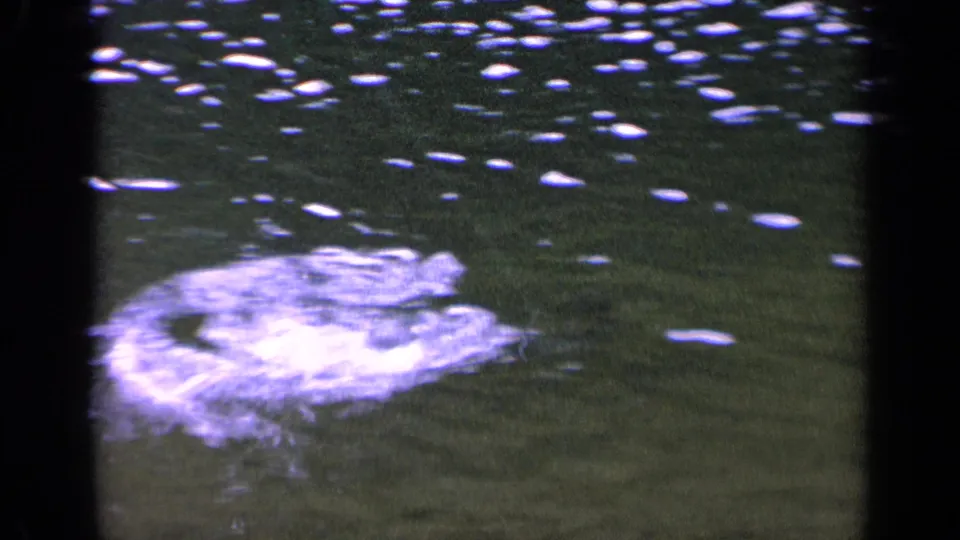 1963 Washington home-movie frame showing a pale disturbance on clear rippling water with small bright surface reflections.