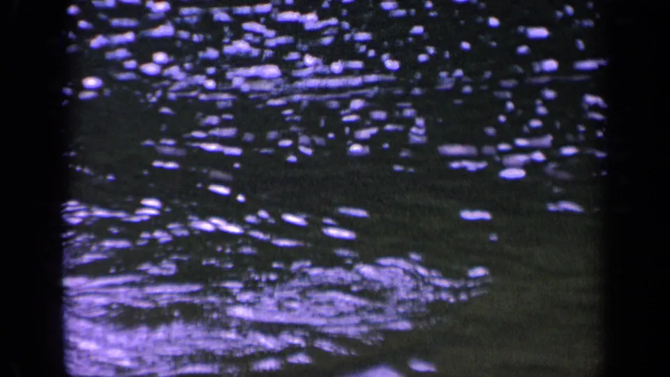 8mm frame from the 1963 Washington clip showing textured water, clustered light reflections, and a pale ripple near the bottom.