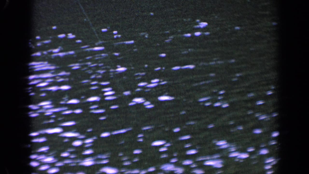 1963 Washington 8mm frame showing rippled lake water with scattered bright reflections and dark frame edges from the film scan.