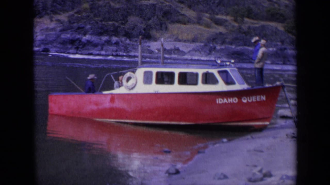 1963 Washington 8mm frame showing the red and cream IDAHO QUEEN boat moored near rocks, with men around the cabin and shore.