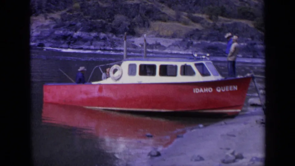 1963 Washington 8mm frame showing the red and cream IDAHO QUEEN boat moored near rocks, with men around the cabin and shore.