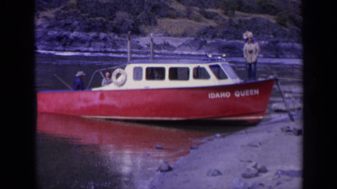Final 1963 Washington frame shows the red and cream IDAHO QUEEN along the rocky shoreline, with men visible near the cabin and stern.