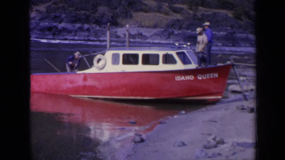 The final visible boat frame shows the Idaho Queen at the shoreline, with a man standing by the stern and others near the bow and cabin.