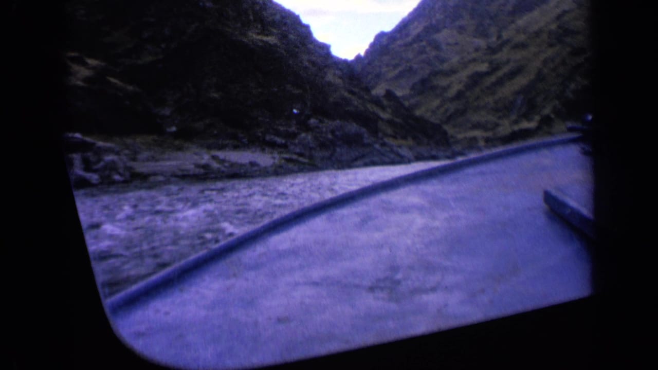 1963 Washington 8mm frame with a tilted first-person boat view across rushing river water toward dark, steep mountain sides.
