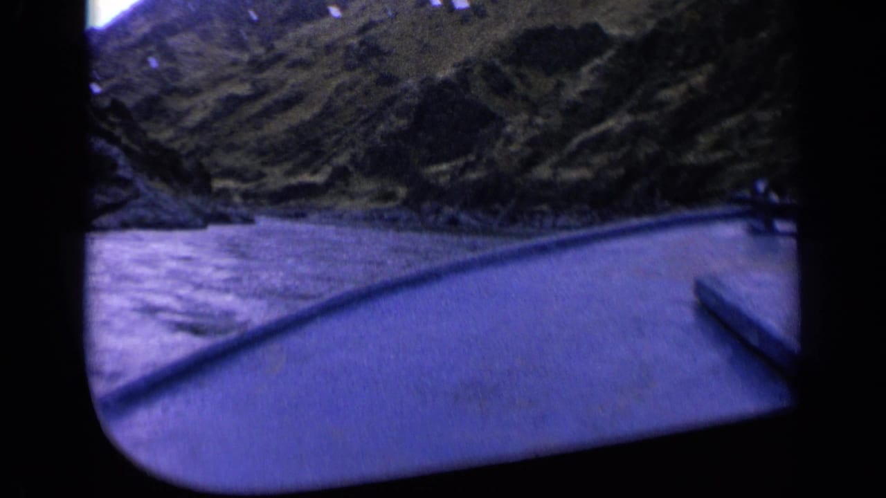 1963 Washington 8mm frame showing a boat-side view across water toward a rugged wooded hillside.
