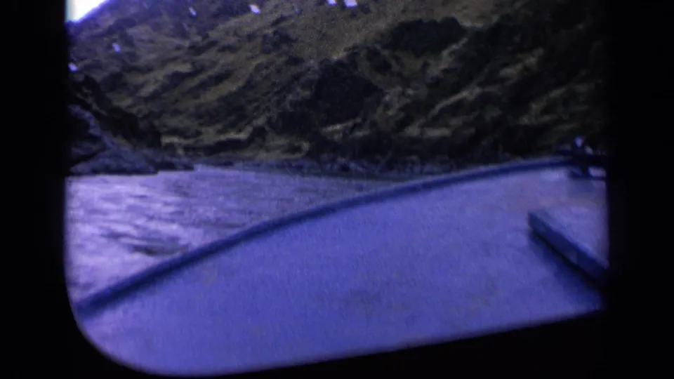 1963 Washington 8mm frame showing a boat-side view across water toward a rugged wooded hillside.