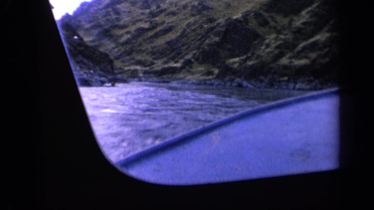 Vintage 8mm boat POV from Washington, 1963, looking over blue-painted boat trim toward water and hillside.