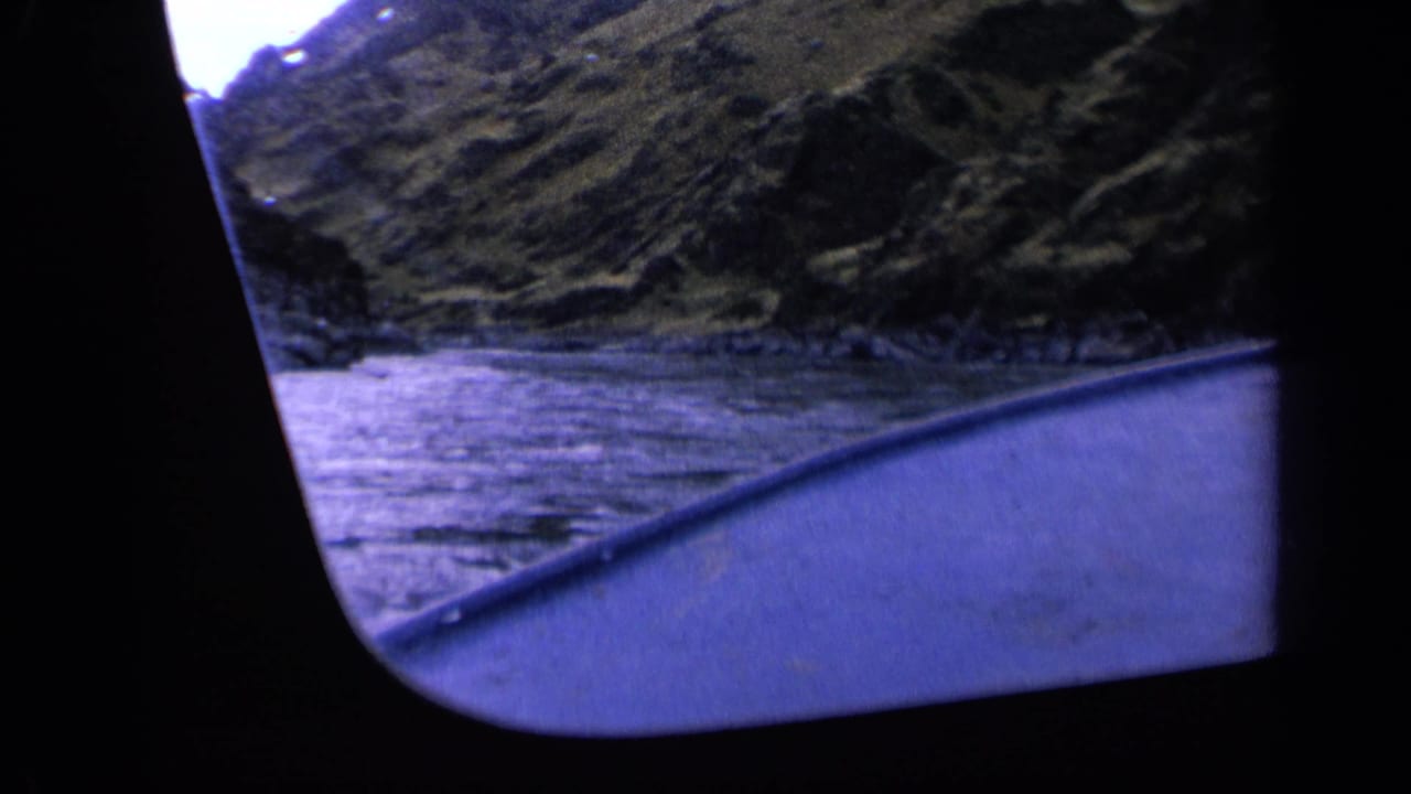 Washington 1963 home-movie frame with boat trim, rippled water, and a steep natural shoreline.
