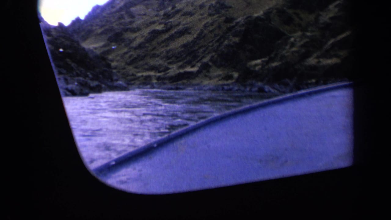 Handheld 8mm view from a vessel on a Washington river, with blue water, dark frame edges, and steep hillside shore.