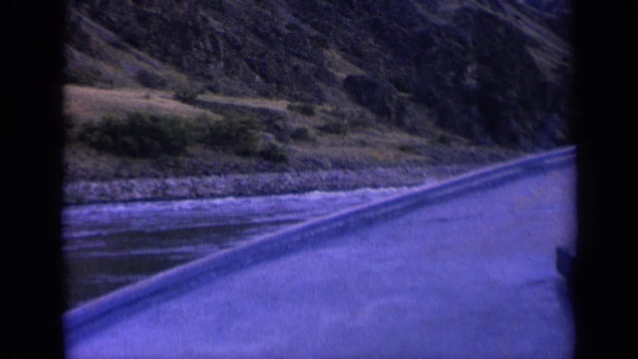 The final frame shows the roadside edge beside a river, with white-capped water, bushes, rocky bank, and mountain slope in Washington footage.