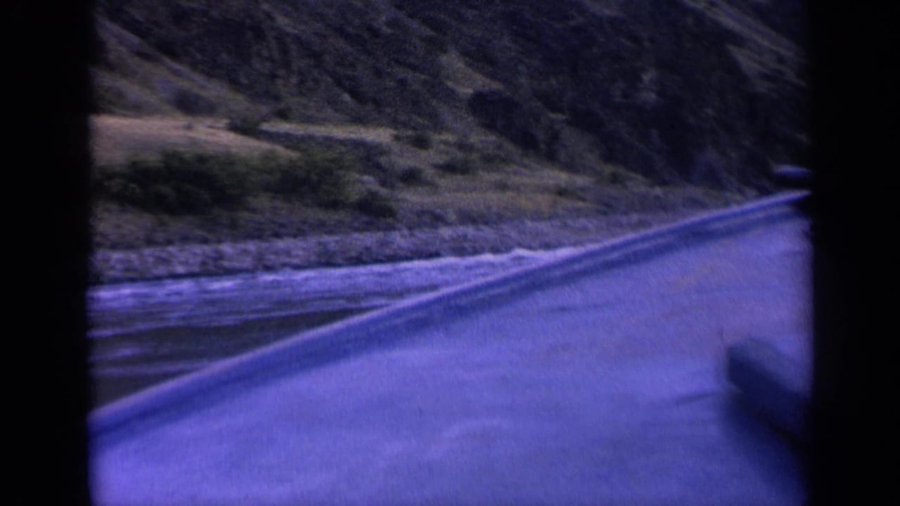 Boat edge and wake moving through a narrow waterway below rocky hills.