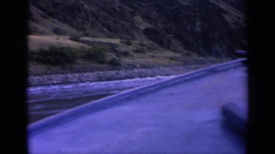 1963 Washington 8mm frame showing a boat-side view across water toward steep, rocky slopes with sparse vegetation.