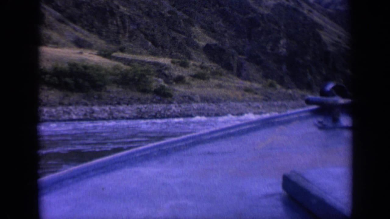 Boat wake stretches across water toward a rocky shore and hillside.